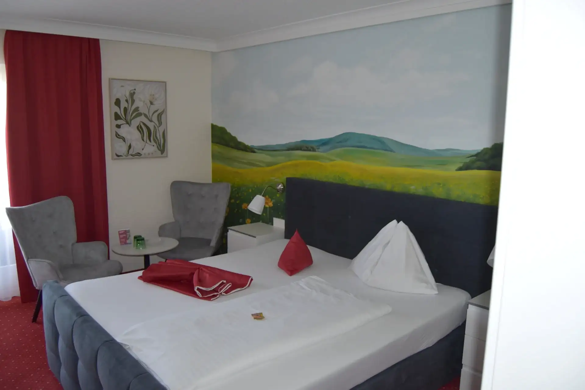 Doppelzimmer mit Landschaftswandbild, gepolstertem Bett und zwei grauen Sesseln