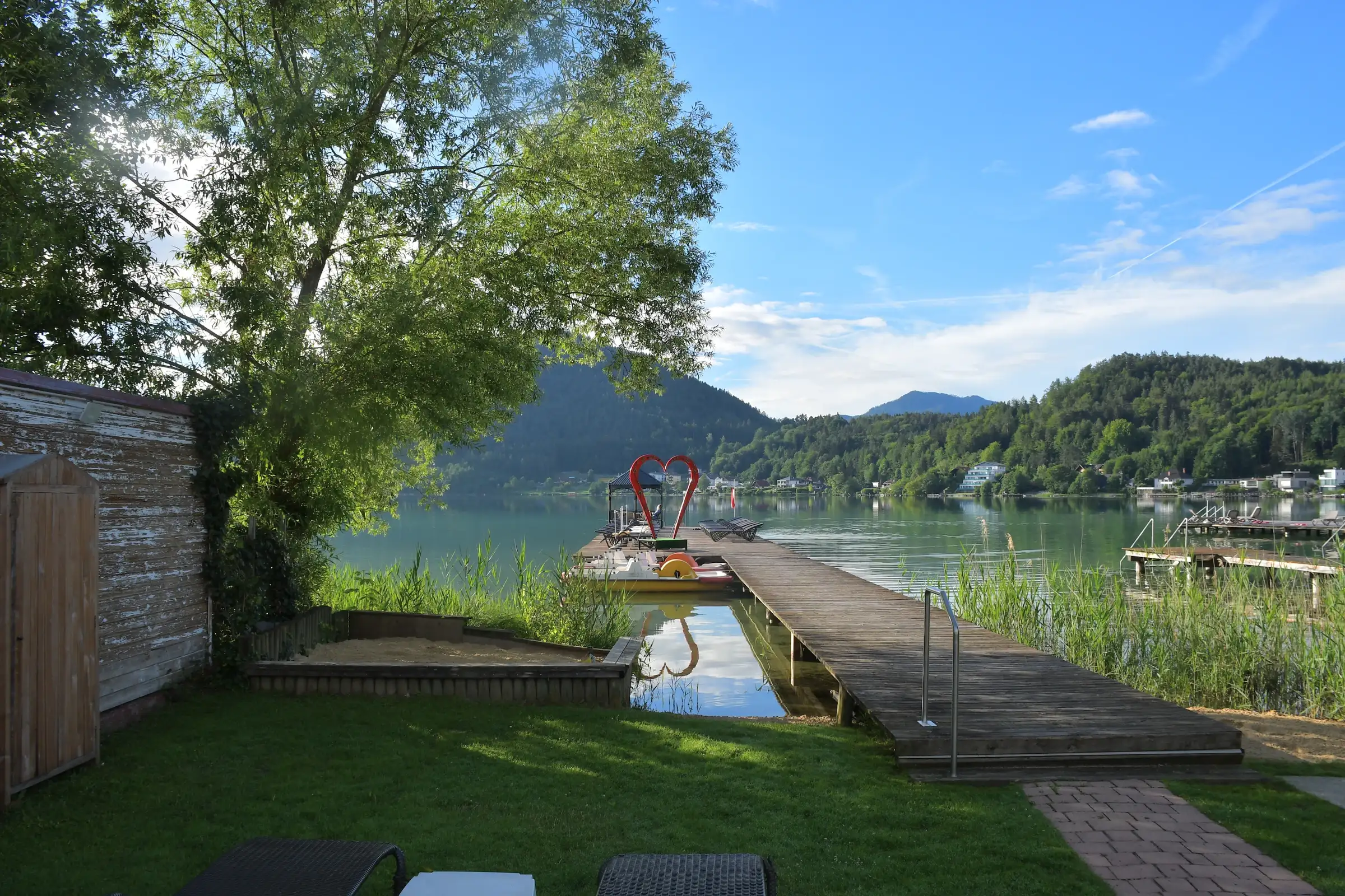 Holzsteg mit rotem Herz und grüner Liegewiese am Klopeinersee